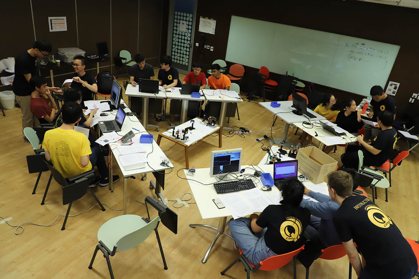 Overhead view of groups participating in QKD workshop, arranged at four tables in a diamond shape with equipment at lower height in the centre.